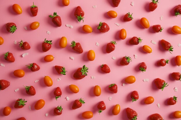 Rijpe smakelijke aardbeien, verse oranje cumquat en witte kokosnootvlokken die op roze muur worden geïsoleerd. Heerlijk fruit voor uw voeding. Schoon eten, lekkere snack, zomertijd concept. Uitzicht van boven