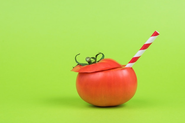 Rijpe tomaat met een rode cocktailbuis op een groene achtergrond.