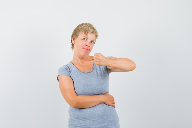 Gratis foto rijpe vrouw die gebalde vuist in grijs t-shirt toont en zelfverzekerd kijkt.