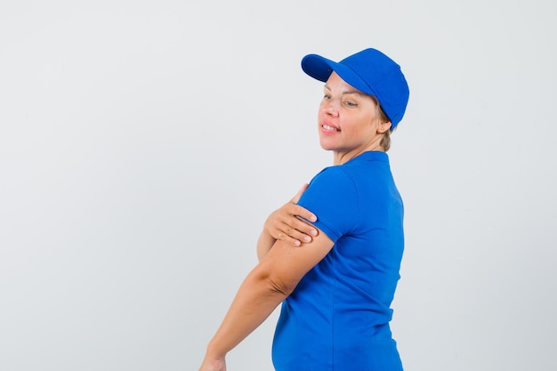 Rijpe vrouw die hand op de andere arm in blauw t-shirt houdt en peinzend kijkt. .