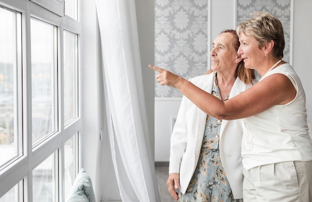 Rijpe vrouw die iets toont aan haar moeder van venster