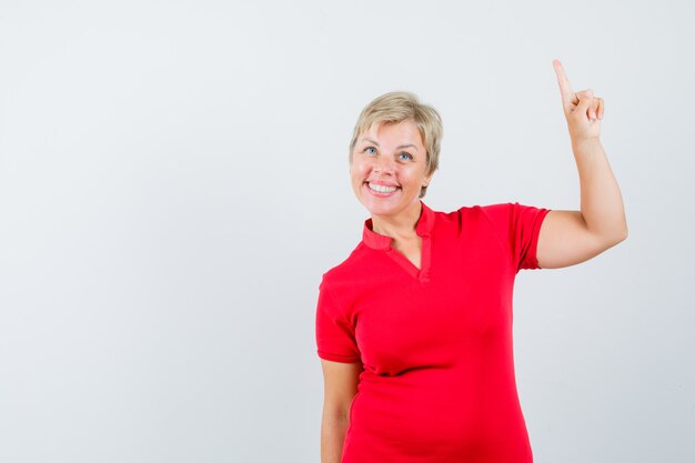 Rijpe vrouw die in rood t-shirt benadrukt en zelfverzekerd kijkt.