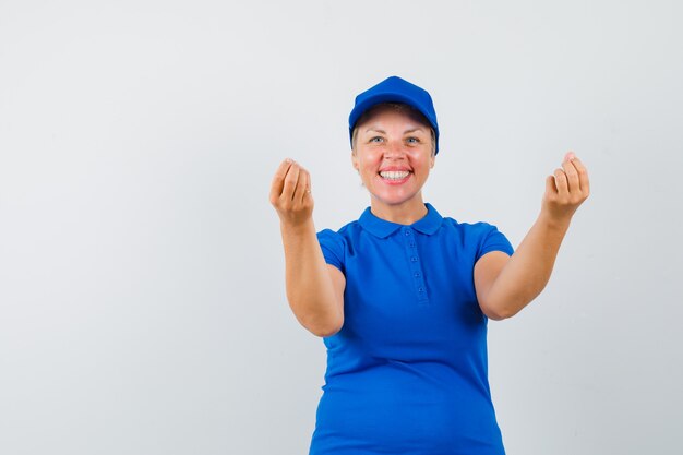 Rijpe vrouw die Italiaans gebaar in blauw t-shirt toont en tevreden kijkt.