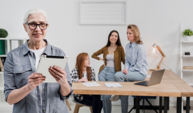 Rijpe vrouw die met glazen een tablet houdt