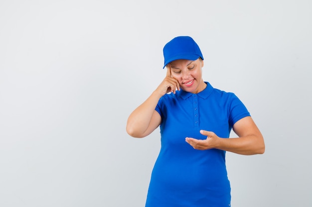 Rijpe vrouw die naar iets keek, deed alsof ze in een blauw t-shirt werd vastgehouden en keek peinzend.