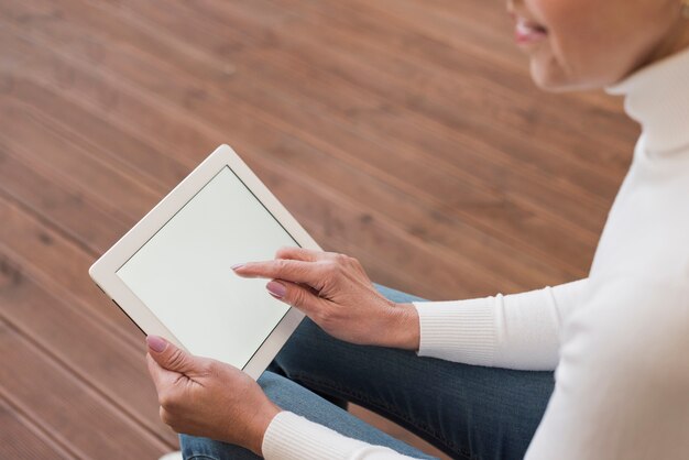 Rijpe vrouw die op haar tablet binnen kijkt