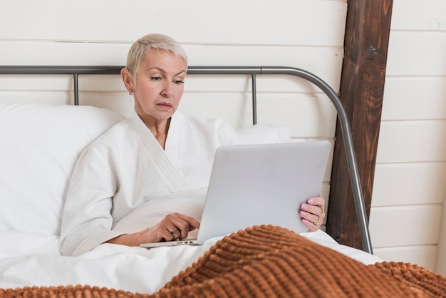 Rijpe vrouw die op laptop in bed kijkt