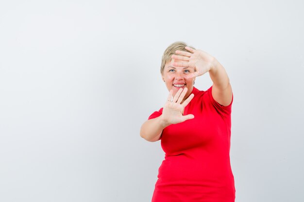 Rijpe vrouw die stopgebaar in rood t-shirt toont en beschaamd kijkt.