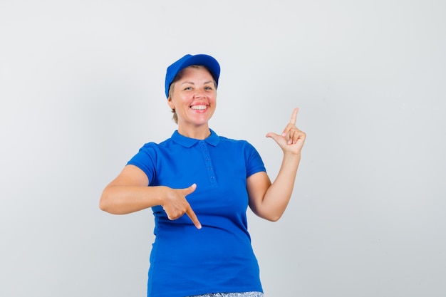 Rijpe vrouw die vingers op en neer in blauw t-shirt richt en vreugdevol kijkt.