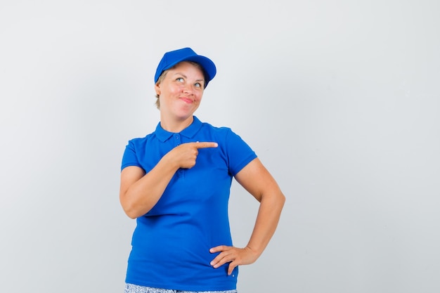 Rijpe vrouw in blauw t-shirt die naar de rechterkant wijst.