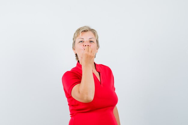 Rijpe vrouw in rood t-shirt die heerlijk gebaar toont en verrukt kijkt