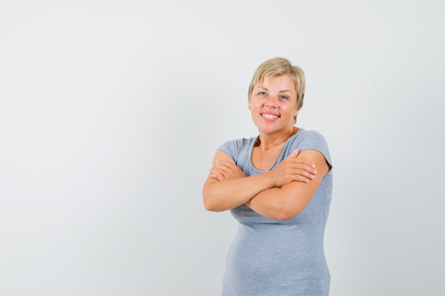 Rijpe vrouw knuffelen zichzelf in grijs t-shirt en ziet er schattig uit.