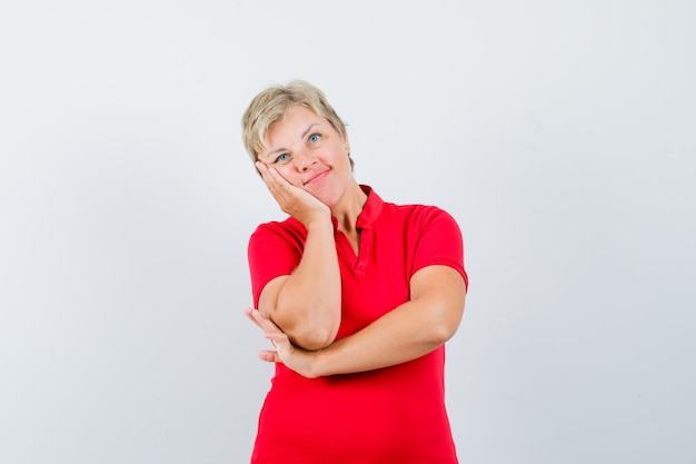 Rijpe vrouw leunende wang op palm in rood t-shirt en ziet er schattig uit.