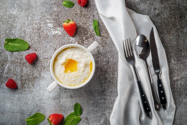Rijst pap met boter en verse aardbeien en frambozen met munt in een witte kop tegen een grijze stenen tafel. een gezond ontbijt in een restaurant
