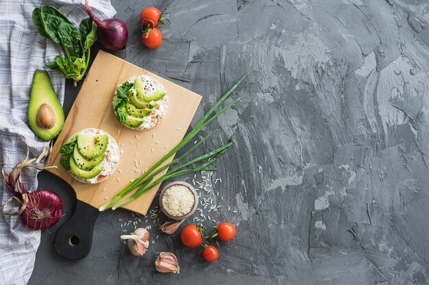 Rijstcake met plakken van avocado over hakbord met ruwe ingrediënten op cementteller