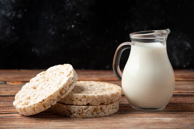 Rijstcrackers en glazen kruik melk op houten tafel.