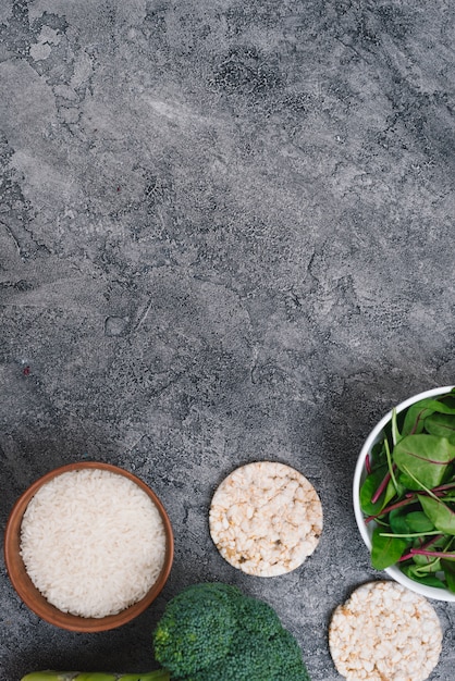 Gratis foto rijstkorrels kommen; gepofte rijstwafels; broccoli en spinazie op grijze verweerde achtergrond