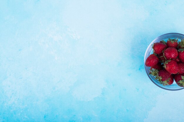 Rode aardbeien in een glazen beker op blauw.