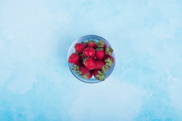 Rode aardbeien in een glazen beker op blauw