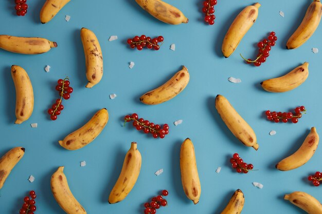 Rode bessen en gele bananen voor het serveren van taarten, broodjesvulling, compotes, sap, huisgemaakt of smoothie. Verzameling van exotisch fruit en rijpe bessen. Plat lag patroon. Lekker zomerfruit