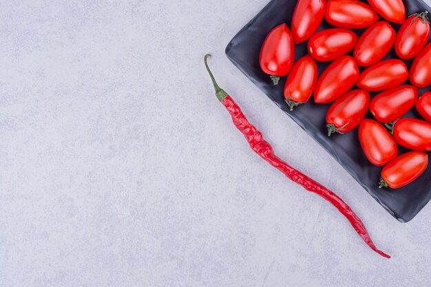 Rode cherrytomaatjes in een zwarte schaal met een chilipeper eromheen.