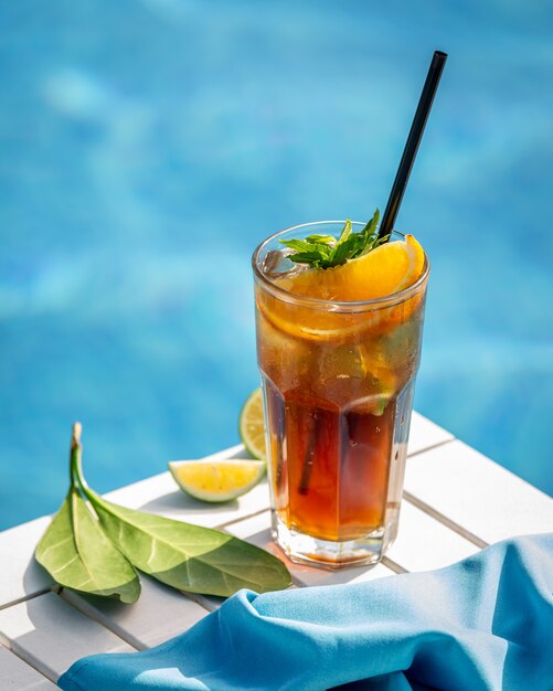 Rode cocktail met citroen, stukjes sinaasappel en hreen kruiden bij een zwembad.