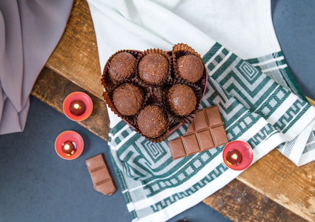 Gratis foto rode doos chocolaatjes, melkachtige chocoladereep en vlammende kaarsen op het tafelkleed