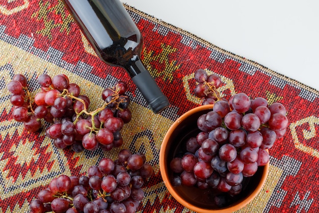 Gratis foto rode druiven in een kom met wijn plat leggen op wit en traditioneel tapijt