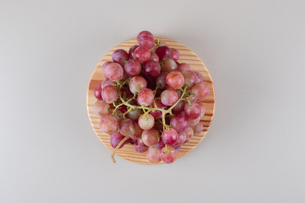 Rode druivenclusters op een houten schotel op marmer