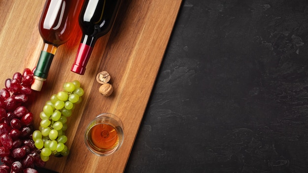 Rode en witte wijnflessen met tros druiven, noten en wijnglas op een houten bord en zwarte achtergrond. bovenaanzicht met kopie ruimte.