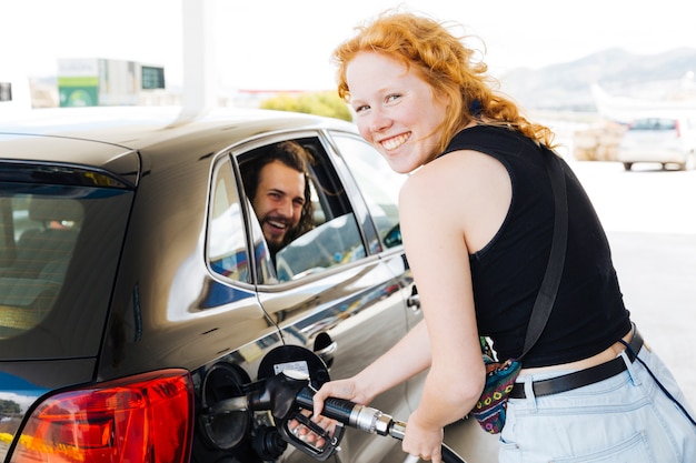 Rode haired jonge vrouwen vullende tank bij benzinepost