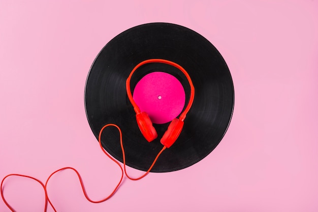 Rode hoofdtelefoon op vinylverslag over de roze achtergrond
