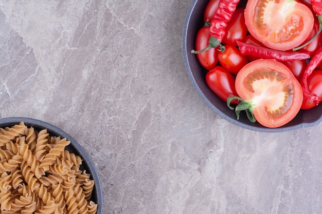 Rode ongekookte pasta's met kerstomaatjes op het marmeren oppervlak