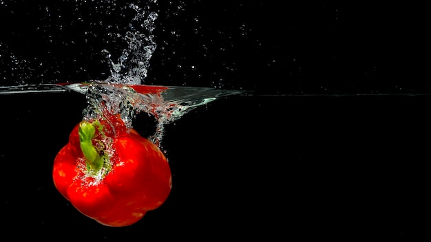 Rode paprika spatten in water over zwarte achtergrond