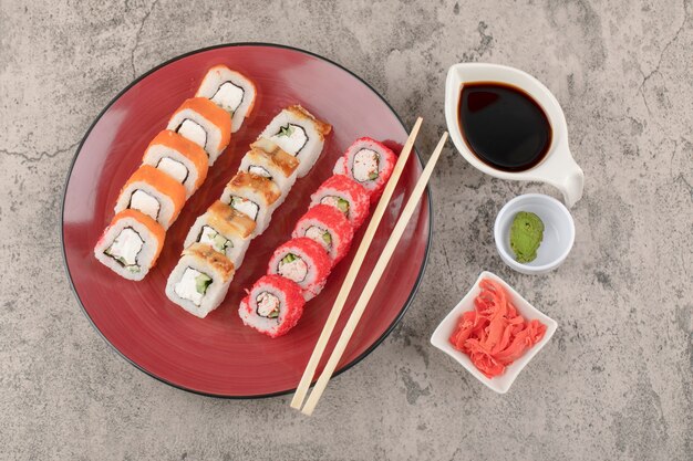 Rode plaat van verschillende sushibroodjes met wasabi en ingelegde gember op marmeren tafel