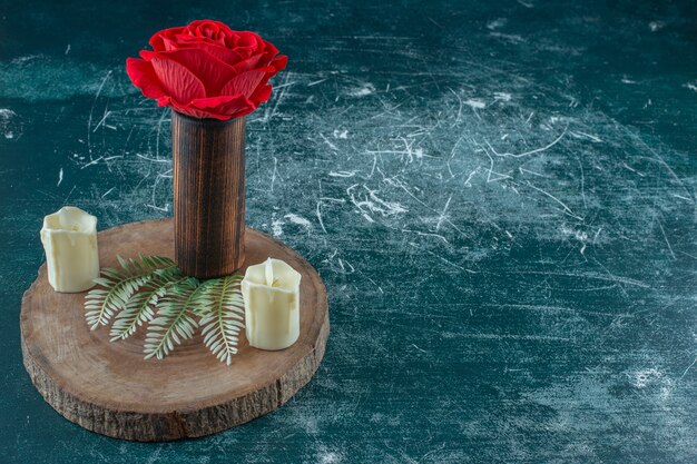 Rode roos in een houten kruik naast kaars op een bord, op de witte achtergrond.