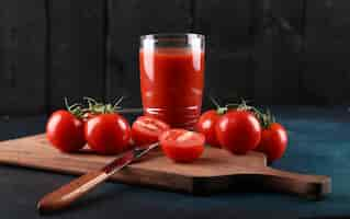 Gratis foto rode tomaten en een glas sap op een houten bord.