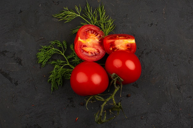 Rode tomaten vers rijp gesneden samen met Groenen op een grijs bureau