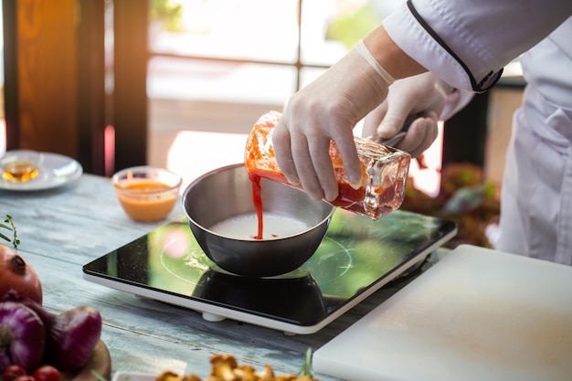 Rode vloeistof giet in pan. hand in handschoen houdt glas vast. tomatensap voor saus. chef-kok mengt ingrediënten.