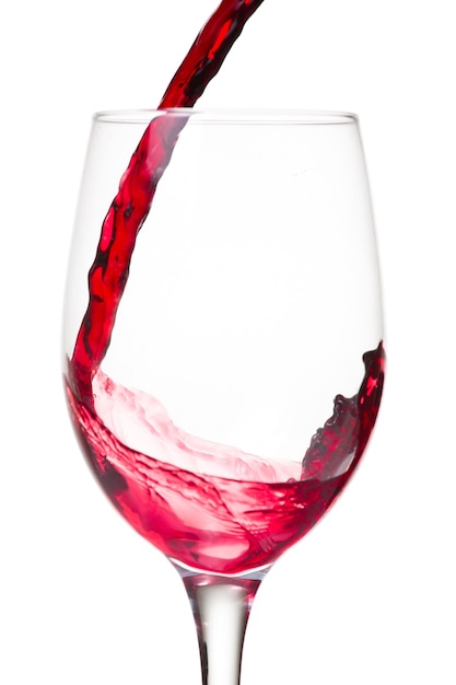 Rode wijn die in een glas wordt gegoten dat op witte muur wordt geïsoleerd