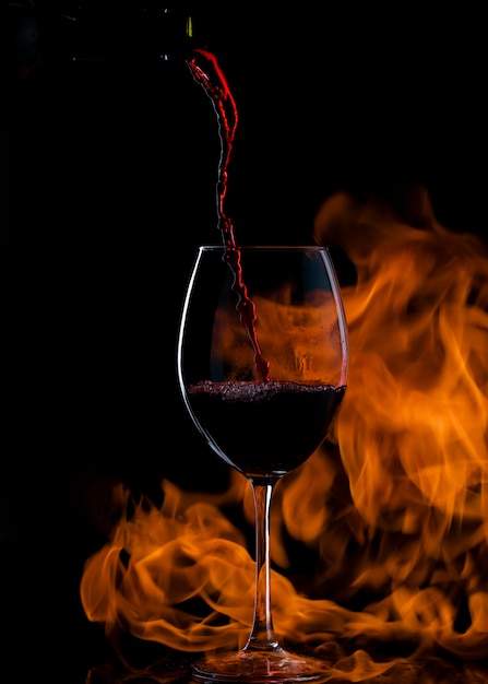 rode wijn in glas gieten met lange steel, met vuur op de achtergrond