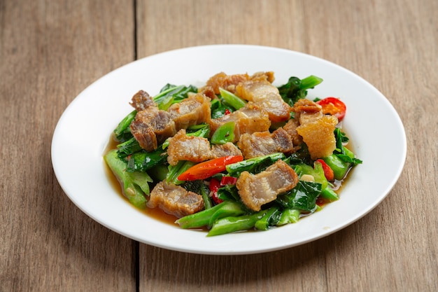 Roergebakken boerenkool, pittig krokant varkensvlees op houten tafel Thais eten concept.