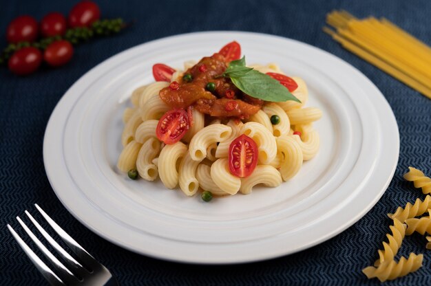 Roergebakken macaroni met tomaat, chili, peperzaadjes en basilicum in een witte schotel.