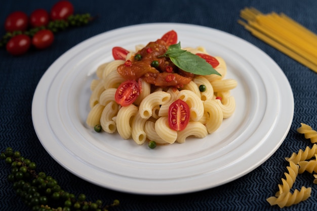 Roergebakken macaroni met tomaat, chili, peperzaadjes en basilicum in een witte schotel.