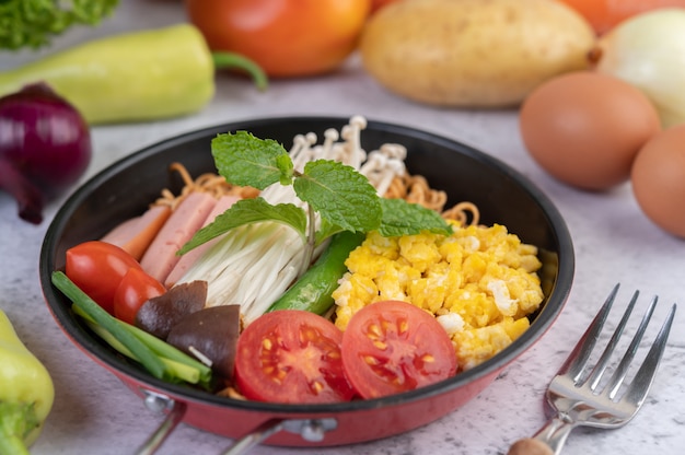 Roergebakken noedels die mais, champignons, tomaat, worst, edamame en lente-uitjes in een koekenpan combineren.
