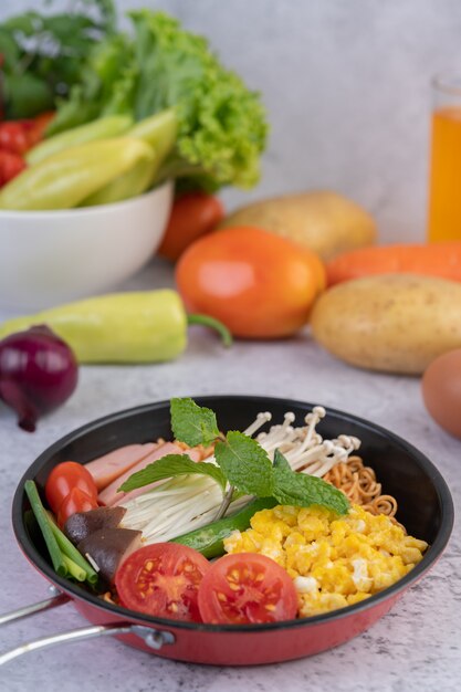 Roergebakken noedels die mais, champignons, tomaat, worst, edamame en lente-uitjes in een koekenpan combineren.