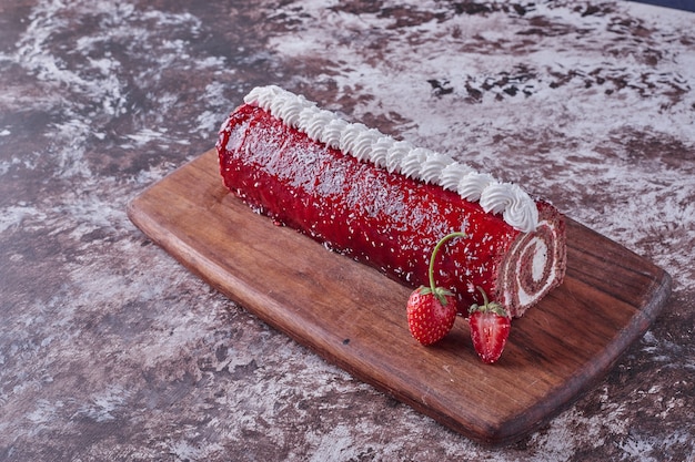 Rol cake met rode marmelade erop op een houten bord met bessen eromheen.