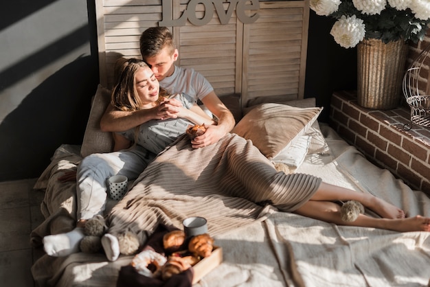 Romantisch jong paar die elkaars hand met ontbijt op bed houden