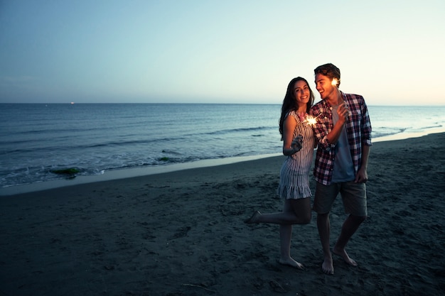 Romantisch koppel met sparkler bij een zonsondergang strand