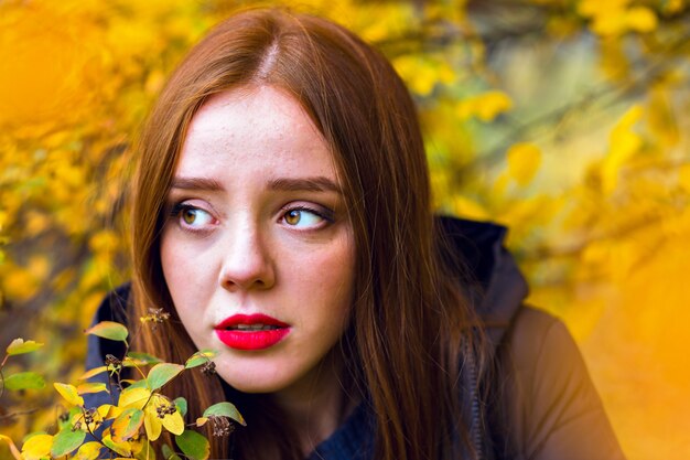 Romantisch meisje met glanzend steil haar wegkijken, verstopt achter gele bladeren. Close-up buiten portret van eenzame brunette vrouwelijke model poseren in herfst park.